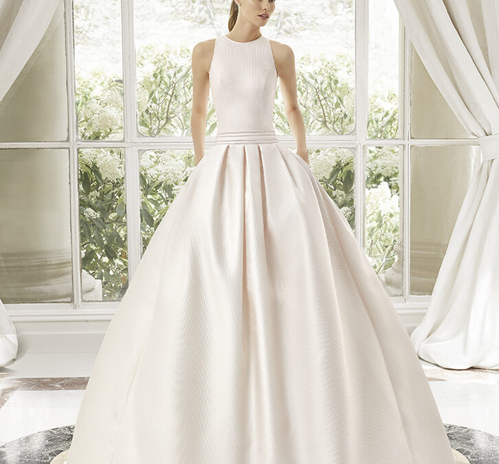 Vestido de noiva de duas peças, de corte direito e estilo moderno, elaborado com crepe. Exiba um decote quadrado, costas descobertas, alças com laço, um corpete com adorno cut out e uma capa de georgette fina. Um conjunto de tendência Rosa Clará Couture.