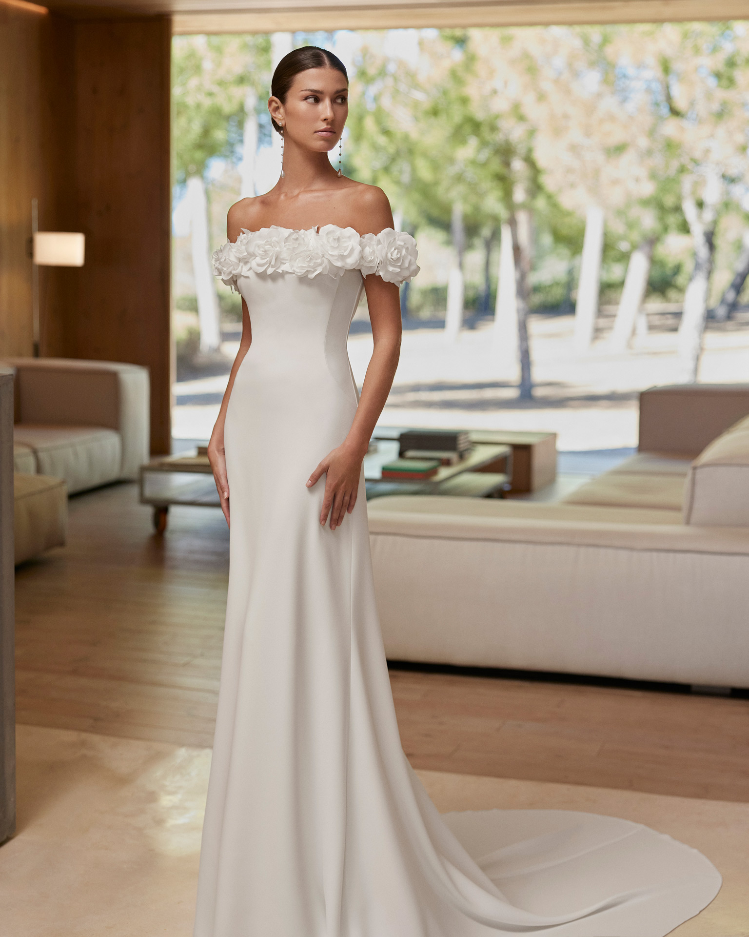 Vestido de noiva de corte sereia e estilo simples, confecionado com crepe elástico. Apresenta um decote caicai com uma flor de adorno. Um modelo exclusivo Rosa Clará.