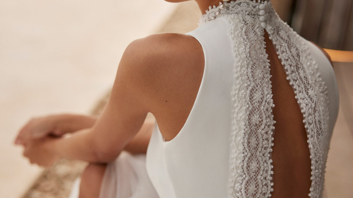 Vestido de noiva de corte evasé e estilo fluido, realizado em tule suave enriquecido com renda e brilhantes. Apresenta um decote halter, umas costas com abertura e uma saia com abertura lateral. Um delicado modelo Rosa Clará.