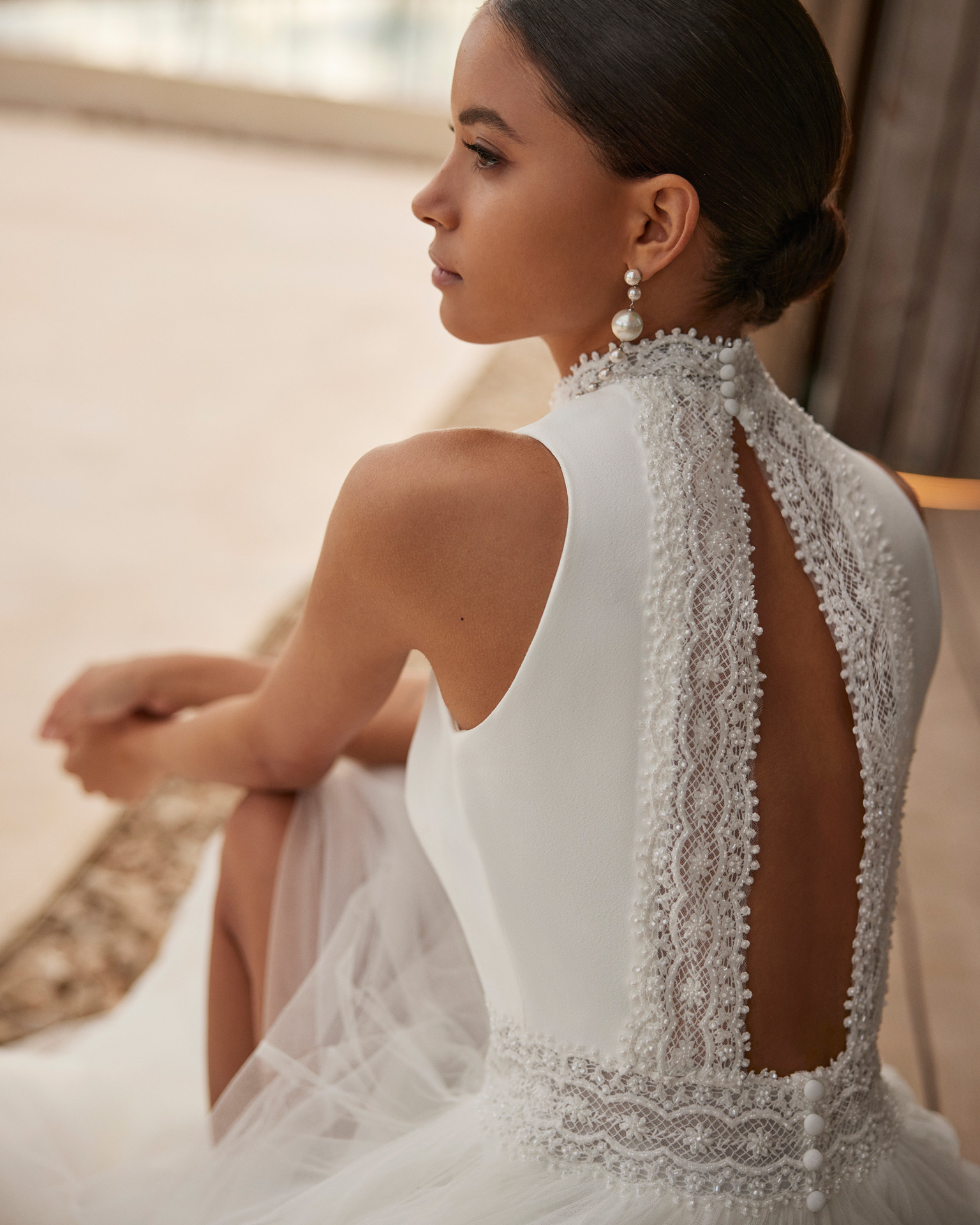 Vestido de noiva de corte evasé e estilo fluido, realizado em tule suave enriquecido com renda e brilhantes. Apresenta um decote halter, umas costas com abertura e uma saia com abertura lateral. Um delicado modelo Rosa Clará.