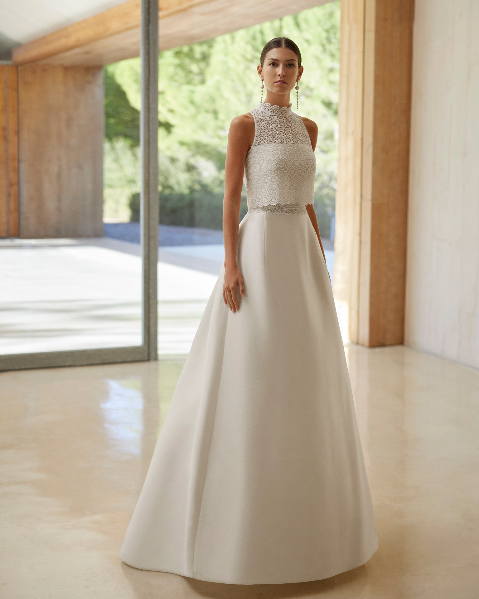 Vestido de noiva de três peças, silhueta em linha A e estilo romântico, confecionado com tecido Sienna. Mostra um decote caicai com um casaco de renda e brilhantes. Completa-se com uma cauda removível. Um conjunto em tendência Rosa Clará.