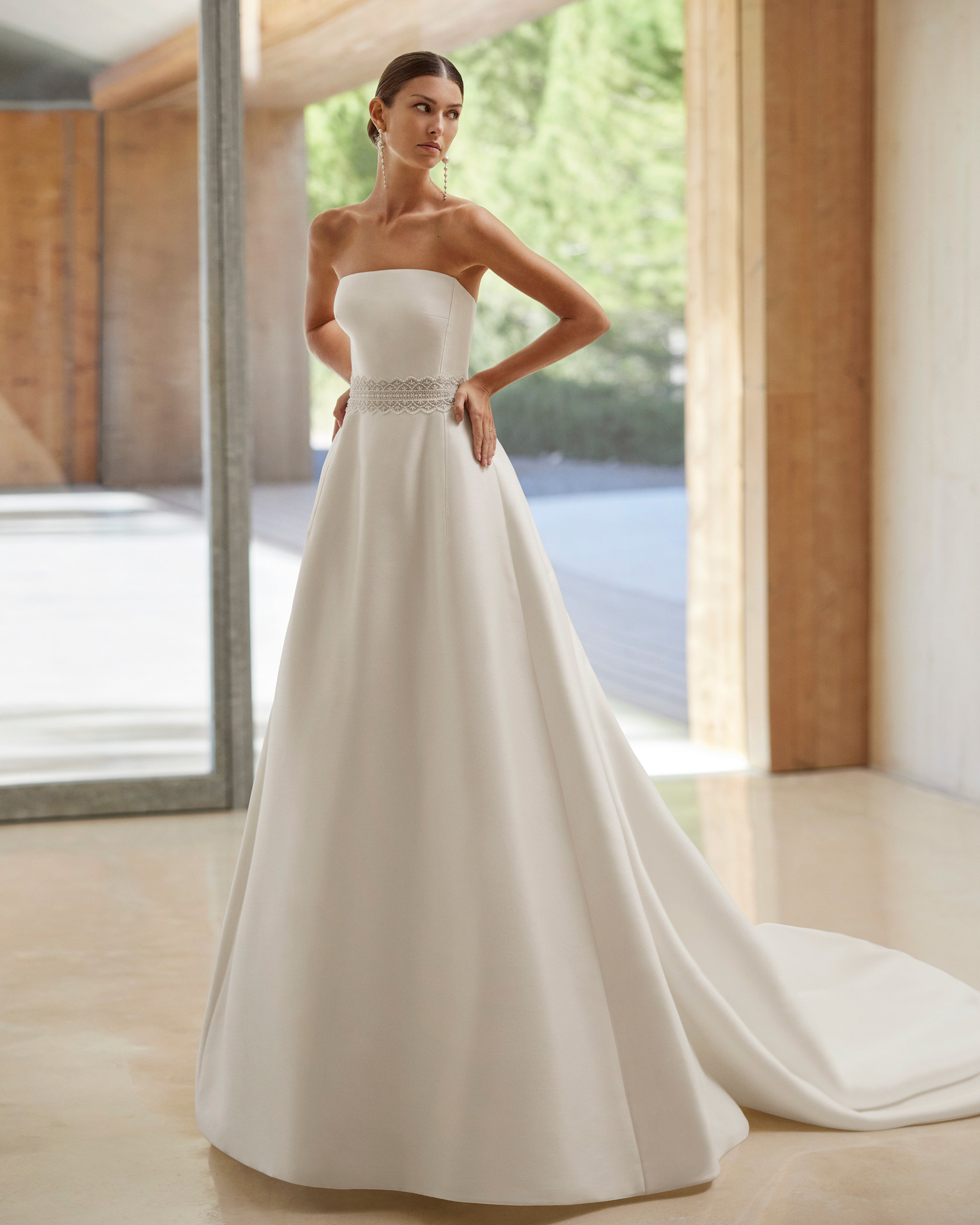 Vestido de noiva de três peças, silhueta em linha A e estilo romântico, confecionado com tecido Sienna. Mostra um decote caicai com um casaco de renda e brilhantes. Completa-se com uma cauda removível. Um conjunto em tendência Rosa Clará.