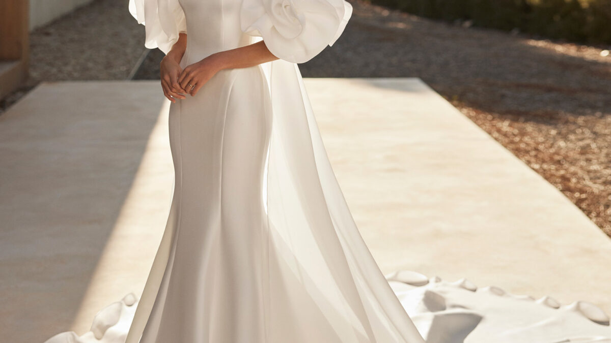 Vestido de noiva de duas peças, corte sereia e estilo elegante, confecionado com mikado elástico. Deslumbra com um decote caicai e um sobretudo de garza. Um conjunto em tendência Rosa Clará.