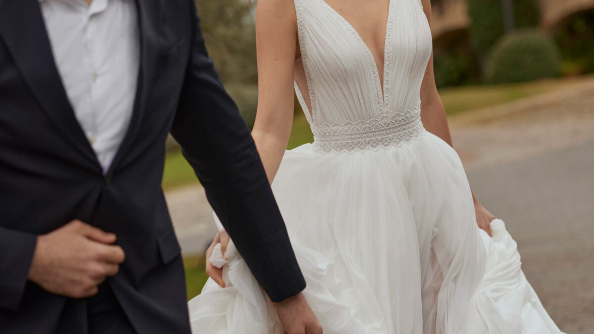 Vestido de noiva comprido, de corte reto e estilo boémio, confecionado em muss combinado com bordado. Completa-se com um decote em V, umas costas em V com alças e uma saia com abertura dianteira.