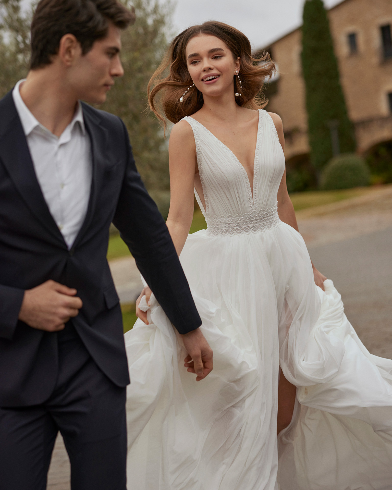 Vestido de noiva comprido, de corte reto e estilo boémio, confecionado em muss combinado com bordado. Completa-se com um decote em V, umas costas em V com alças e uma saia com abertura dianteira.