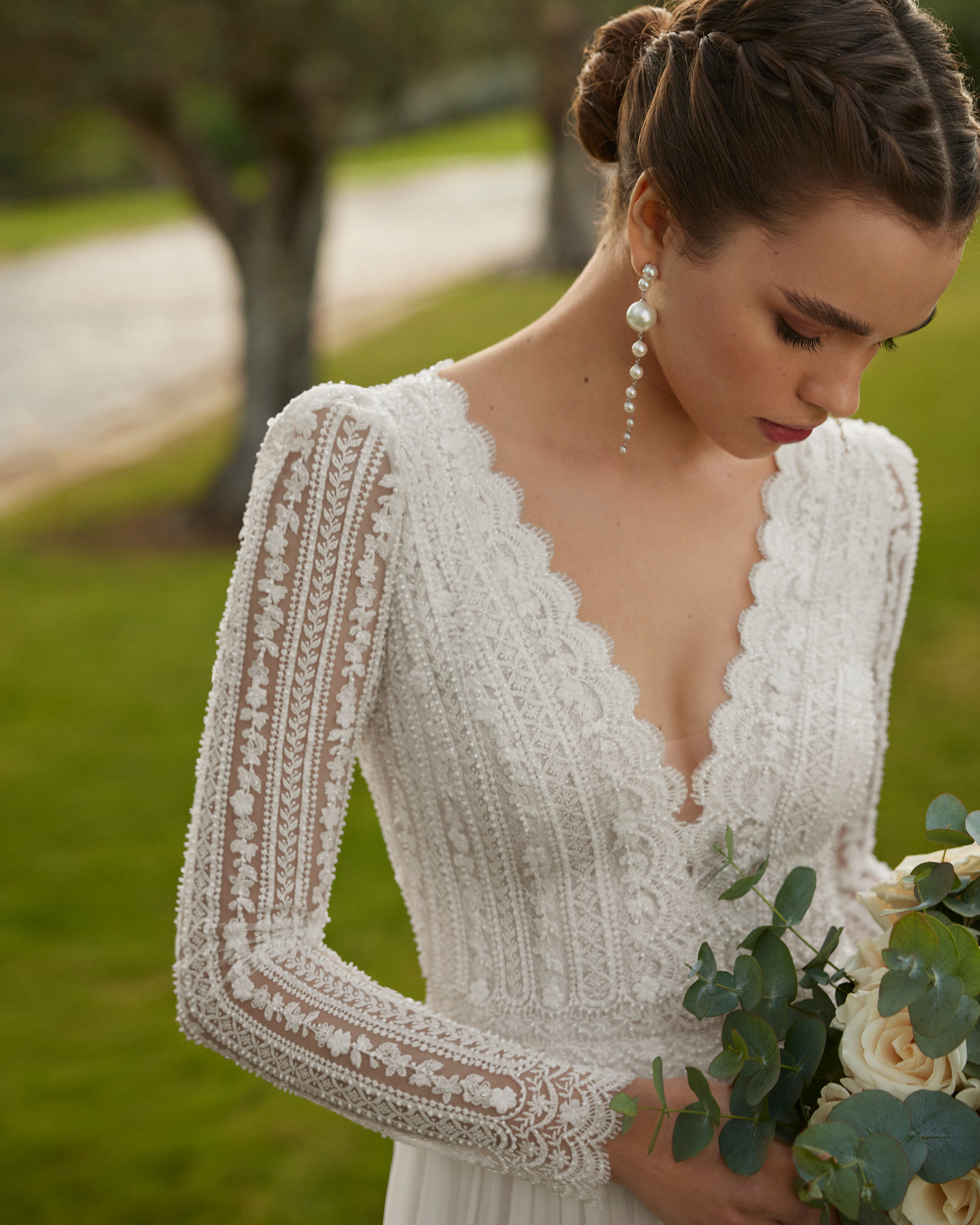 Vestido de noiva comprido, de corte reto e estilo boémio, confecionado com renda e brilhantes e saia em muss. Completa-se com um decote em V, costas fechadas e manga comprida.