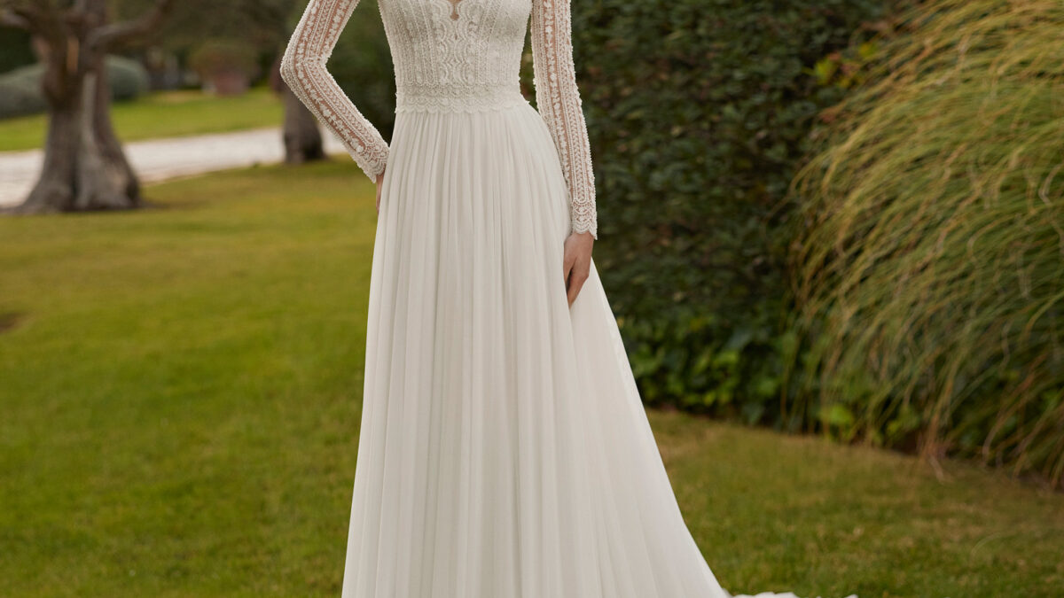Vestido de noiva comprido, de corte reto e estilo boémio, confecionado com renda e brilhantes e saia em muss. Completa-se com um decote em V, costas fechadas e manga comprida.