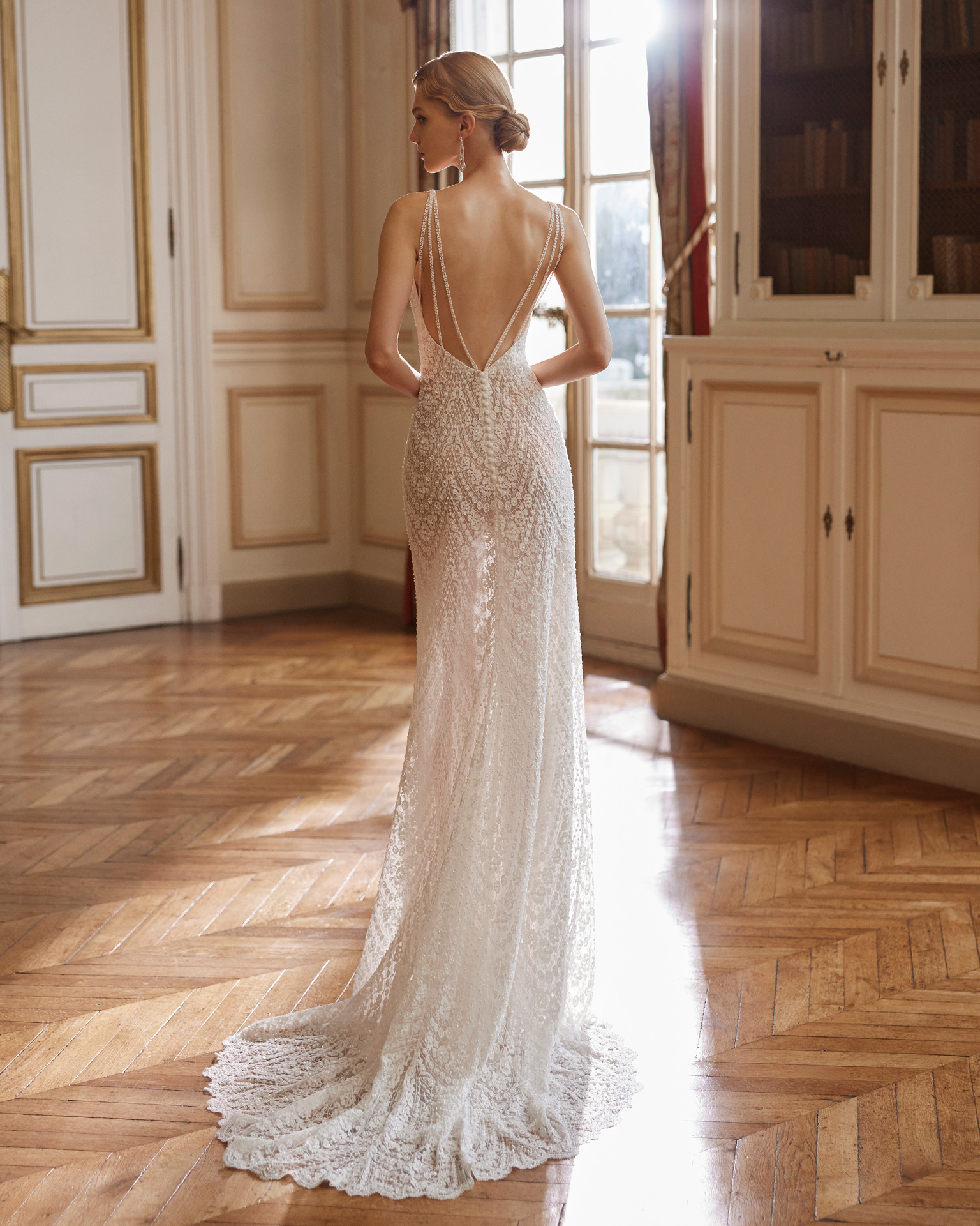 Vestido de noiva de corte sereia e estilo elegante, confecionado com renda e brilhantes. Apresente um decote profundo e umas costas abertas com alças. Exiba um exclusivo fato Rosa Clará Gatsby.
